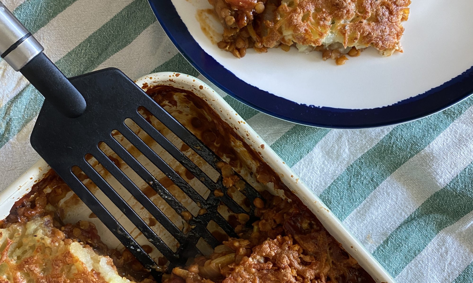 Vegetarian version of Cottage Pie on a green and white stripe cloth next to a plated vegetarian cottage pie